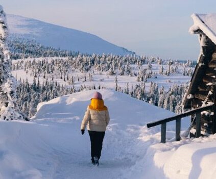 Une femme marchant dans la neige profonde avec des montagnes enneigées en arrière-plan.